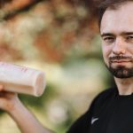 Adult man holding a protein shake outdoors during the day.